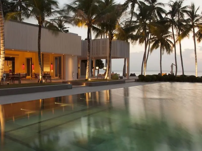 Modern beachfront villa with palm trees and a reflective pool at sunset in the Maldives.